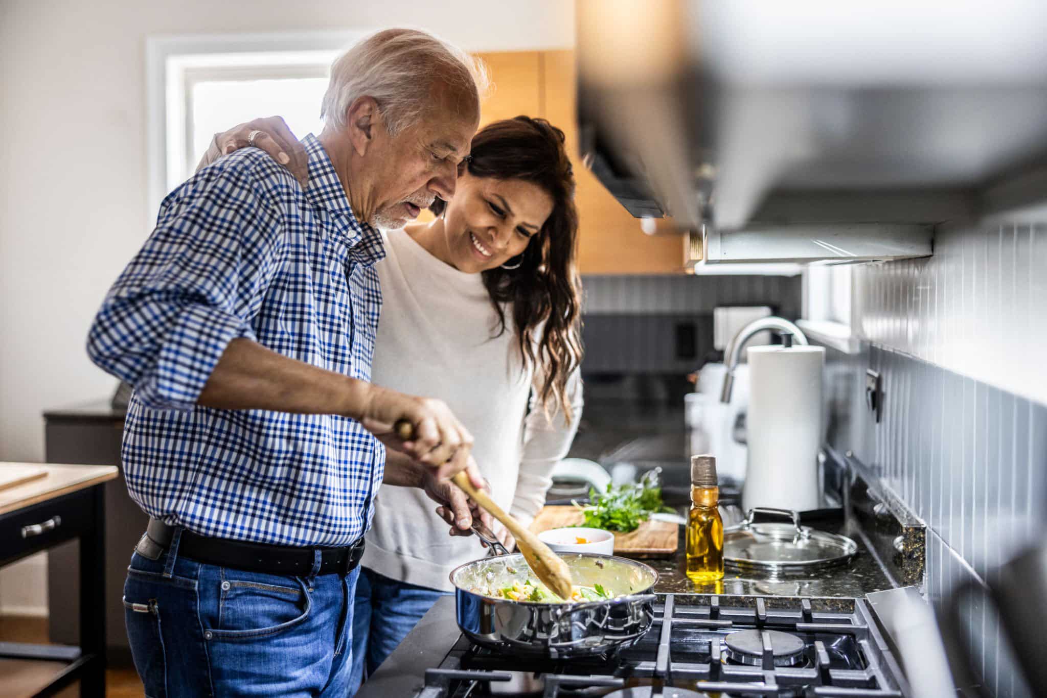 Elderly man and younger woman smiling while cooking together in a modern kitchen